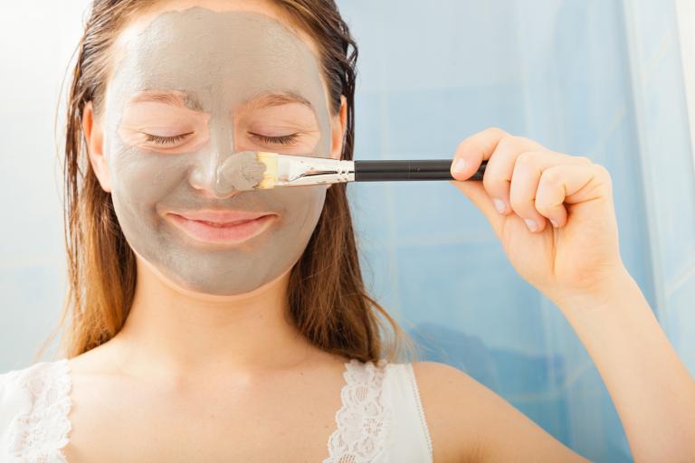 a teenage girl applying a gray mud facial mask