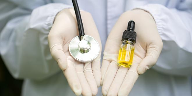 A Dr.'s hands holding a stethoscope and a bottle of CBD oil.