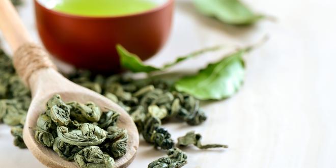 A spoon of dried leaves and a cup of green tea