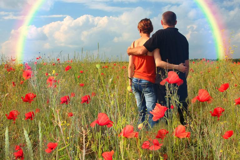 a couple in a field looking toward a rainbow