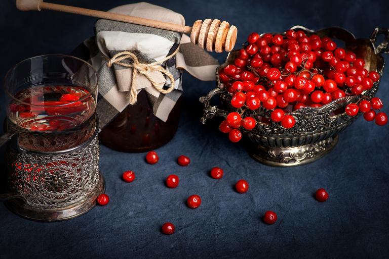 Glass in a silver coaster, a vase with medical berries and bank of honey on a dark background